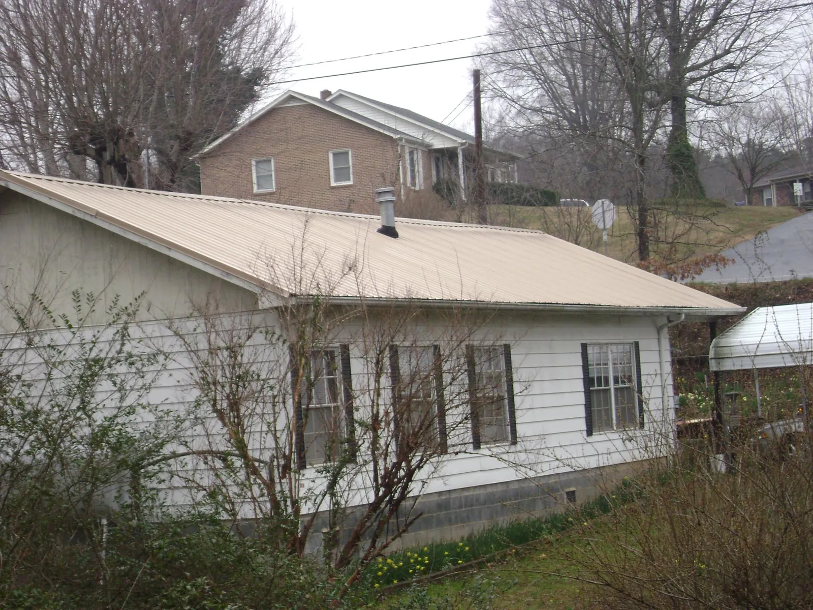 Tan metal roof on a white sided house set into a hillside — Commercial Roofing by Roofing Brothers in Granville